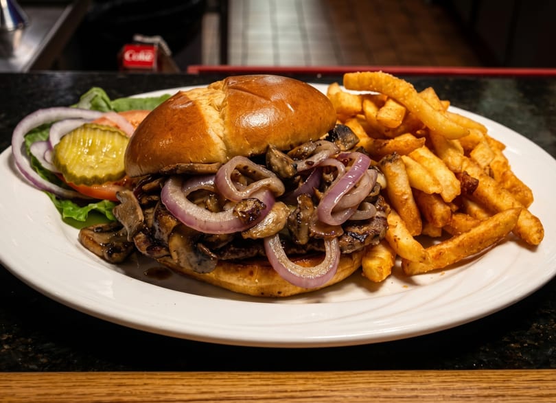A mushroom and onion burger with a side of fries and a small salad on a white plate.